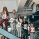 A diverse team standing on an office staircase holding letters that spell "BRAND," representing branding, public relations, and teamwork.